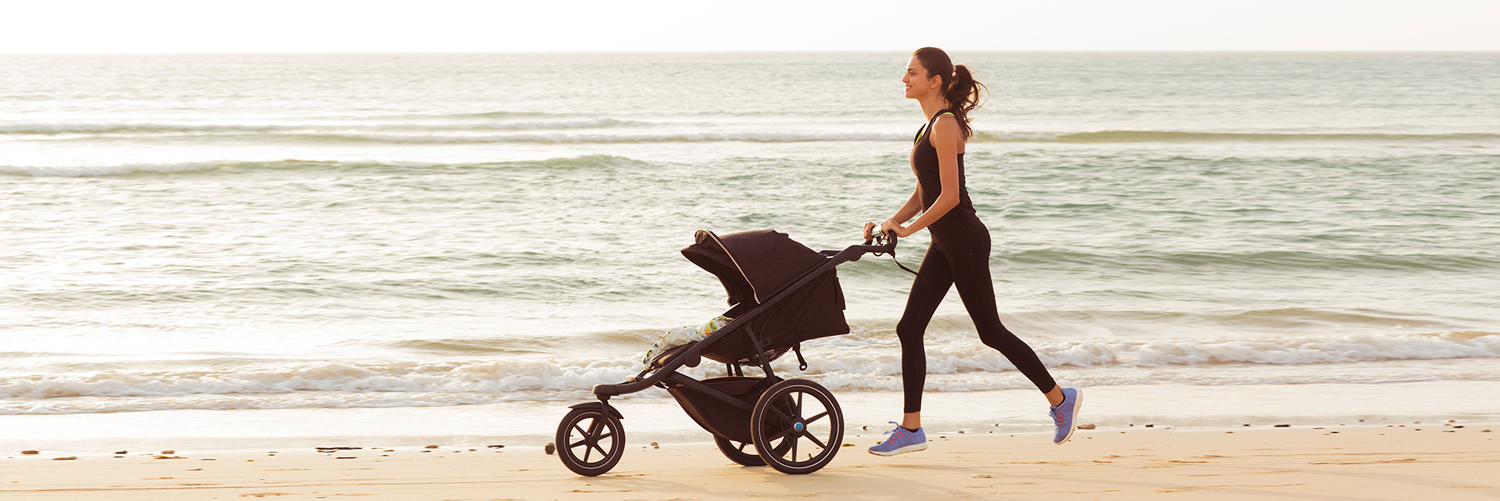 A parent jogging on the beach with a stroller